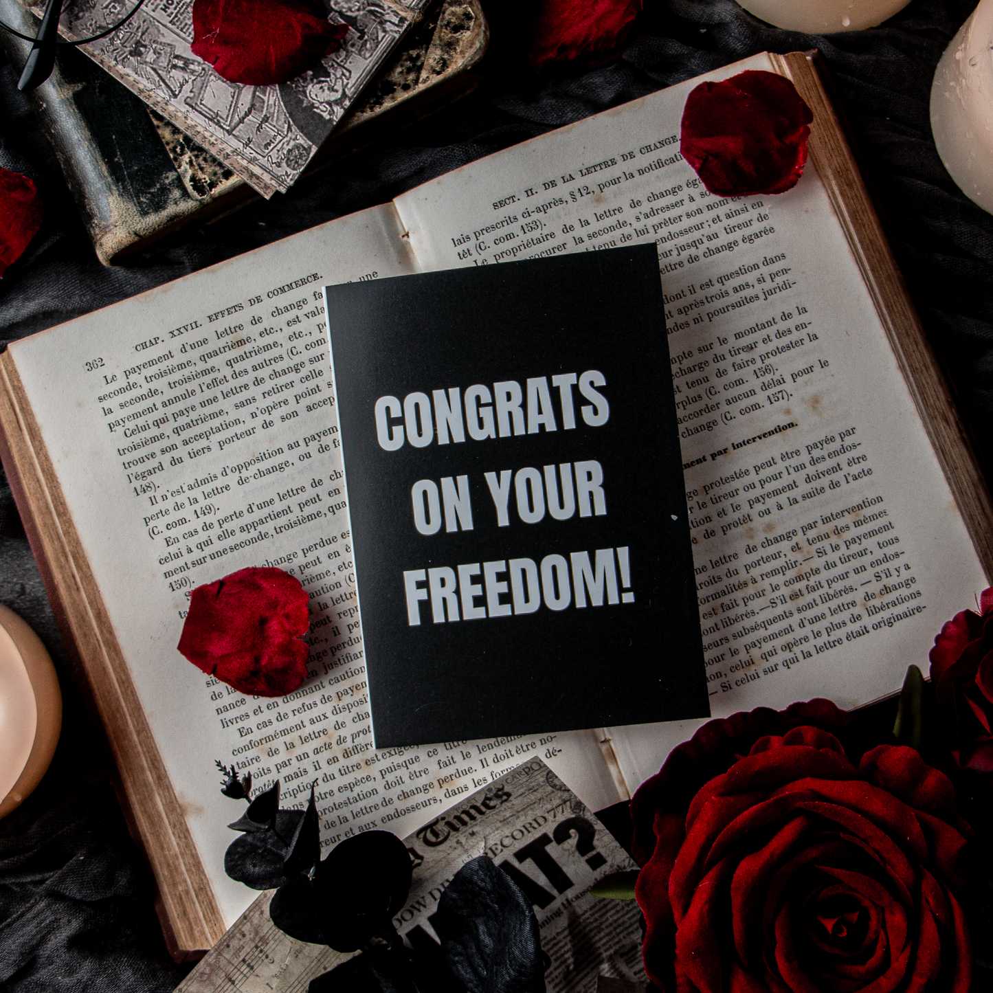 A greeting card with the text 'CONGRATS ON YOUR FREEDOM!' placed on an open book surrounded by rose petals and candles.