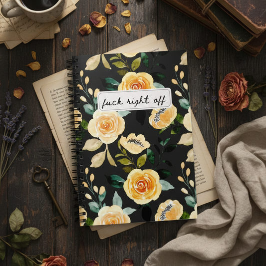 Notebook with floral design and visible text on a wooden surface with coffee and flowers.