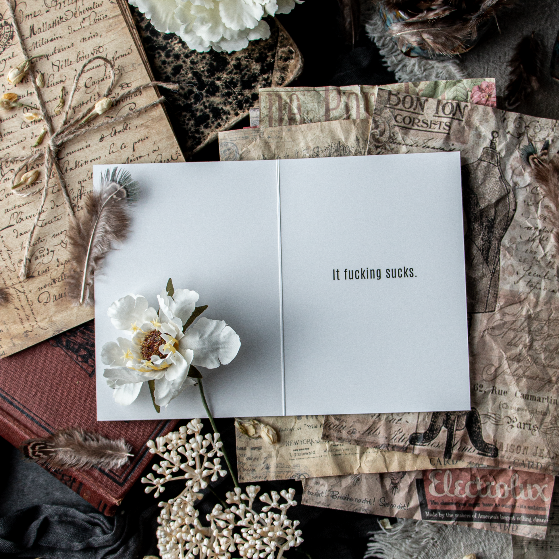 Greeting card with floral design on a textured surface with vintage books and feathers