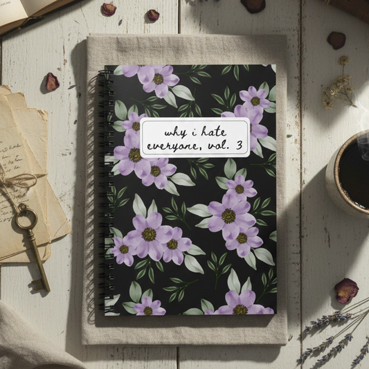 Notebook with floral design and text on a wooden surface with books and coffee.