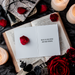 A greeting card with the text 'CONGRATS ON YOUR FREEDOM! HERE'S TO LOW STRESS AND HIGH ALIMONY.' placed on a table with a book, candles, and rose petals around it.