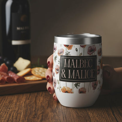 Person holding a 'Malbec & Malice' wine tumbler with a wine bottle and charcuterie board in the background.