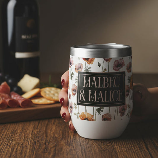Person holding a 'Malbec & Malice' wine tumbler with a wine bottle and charcuterie board in the background.