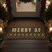 Decorative doormat with 'MERRY AF' text on a wooden porch with Christmas decorations.
