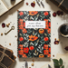 Notebook with floral design on a surface with books, coffee, and flowers.