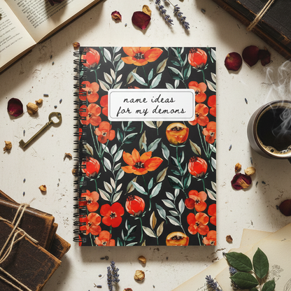 Notebook with floral design on a surface with books, coffee, and flowers.
