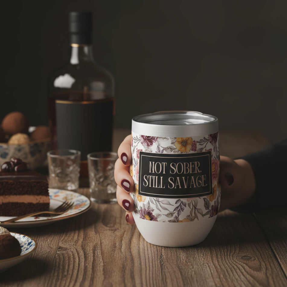 Person holding a mug with 'Hot Sober Still Savage' text on a wooden table with cake and bottle in the background