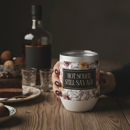 Person holding a mug with 'Hot Sober Still Savage' text on a wooden table with cake and bottle in the background