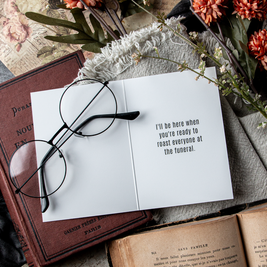 Open book with glasses on top, surrounded by flowers and books, with a humorous quote.