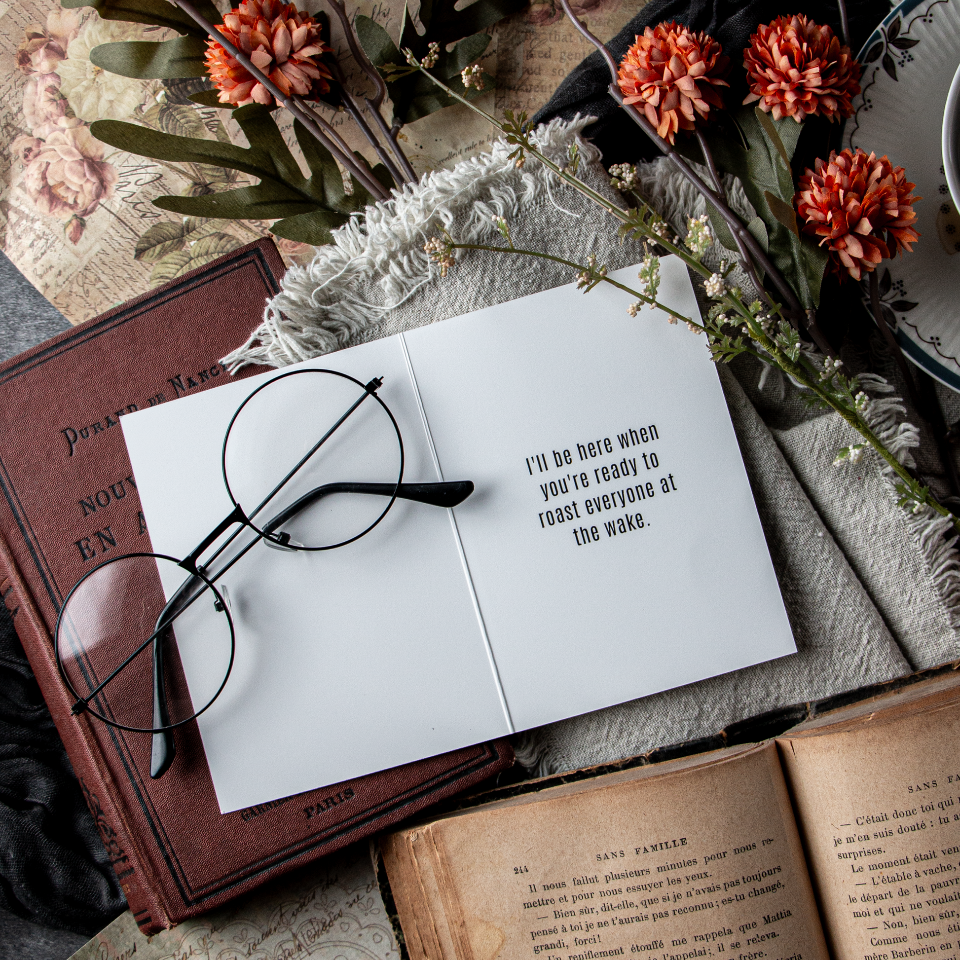 Open book with glasses on top, surrounded by flowers and another open book on a textured surface.