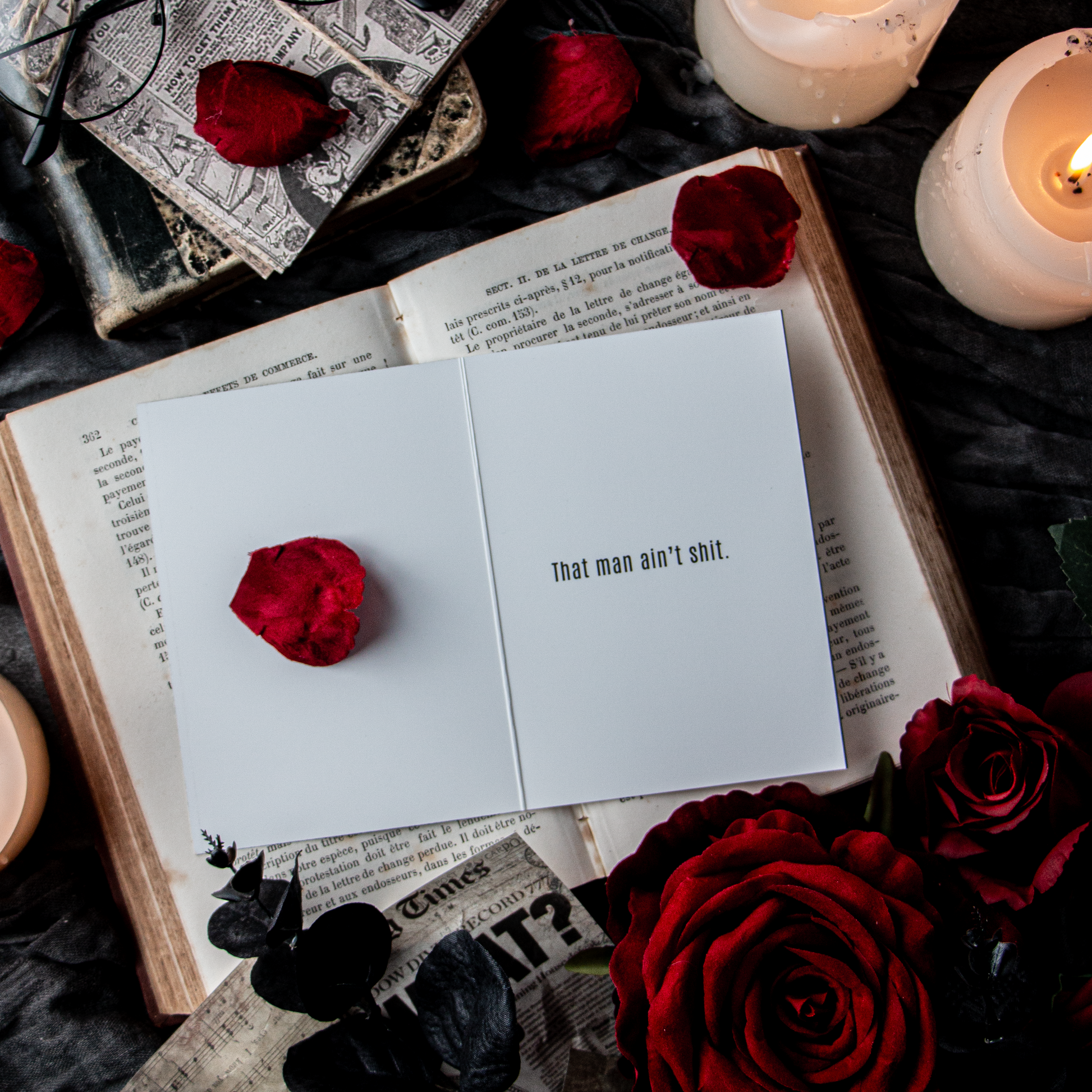 A greeting card with a bold statement placed inside an open book, surrounded by rose petals and candles, depicting a theme of freedom or separation.