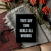 Black sign with 'THEY SAY TIME HEALS ALL WOUNDS' text on a textured surface with flowers and books.